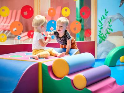 Zwei Kleinkinder spielen auf einem bunten Indoor-Spielplatz mit weichen Formen und Kissen.