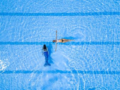 Blick von oben auf einen Schwimmer und eine Roboterpool-Reinigungsmaschine im blauen Schwimmbecken.