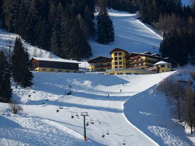 Piste de ski enneigée avec télésiège et plusieurs bâtiments près d'une colline boisée