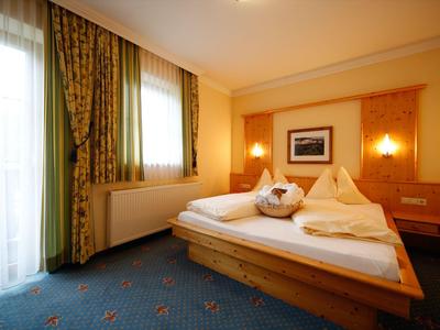 Gemütliches Hotelzimmer mit Doppelbett, Holzmöbeln und großem Fenster mit Vorhängen.