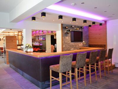 Moderner Hotelbarbereich mit Theke, Barhockern und stimmungsvoller Beleuchtung.
