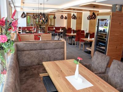 Modernes Restaurant mit Holz- und Polstermöbeln, roten Sitzpolstern und großen Fenstern für viel Licht.