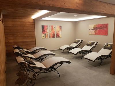 Salle de détente avec six chaises longues blanches, panneaux en bois et œuvres d'art aux murs.