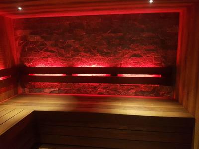 Banc en bois de sauna avec éclairage LED rouge et mur en pierre naturelle en arrière-plan.