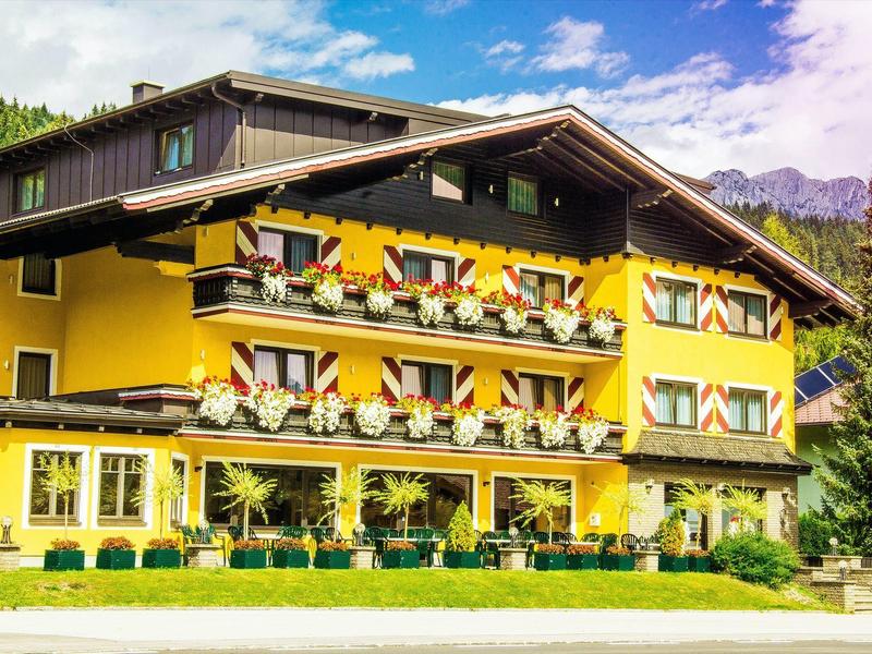 Bâtiment d'hôtel jaune avec des fleurs aux fenêtres dans un paysage montagneux sous un ciel bleu.