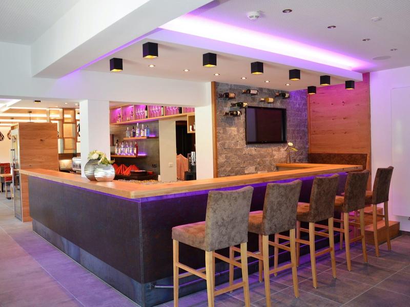 Espace bar d'hôtel moderne avec comptoir, tabourets et éclairage indirect d'ambiance.