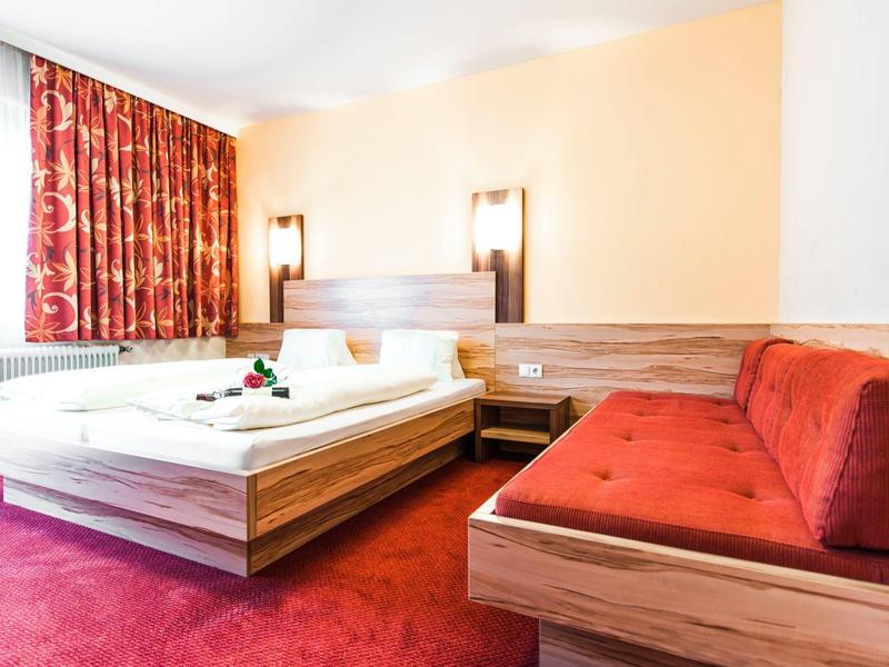 Chambre d'hôtel confortable avec lit double, tapis rouge et canapé rouge à côté du lit.