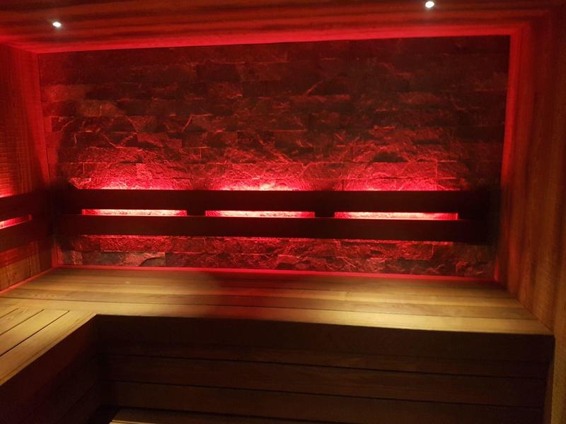 Banc en bois de sauna avec éclairage LED rouge et mur en pierre naturelle en arrière-plan.