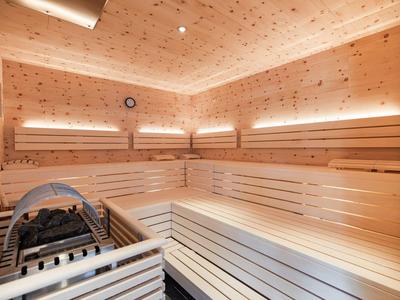 Helle Holzsauna mit mehreren Sitzreihen, Ofen und Beleuchtung an Wänden und Decke.