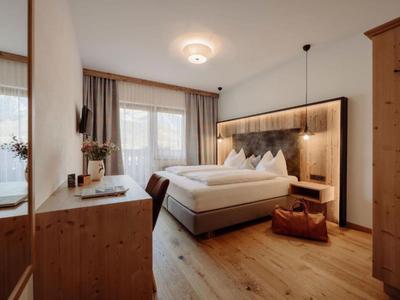 Gemütliches Schlafzimmer mit Holzfußboden, doppeltem Bett, Nachttisch und großem Fenster mit Vorhängen.