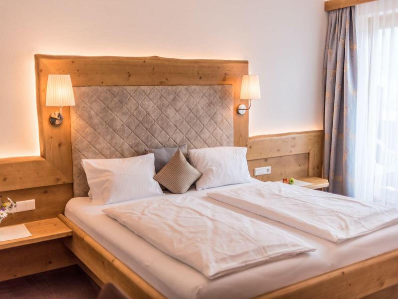 Gemütliches, helles Schlafzimmer mit Doppelbett, Holzmöbeln und großen Fenstern mit Gardinen.