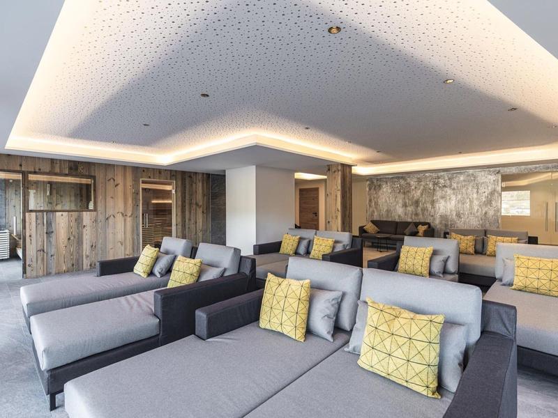 Modernes Wohnzimmer mit grauen Sofas, gelben Kissen, Holzverkleidung und indirekter Deckenbeleuchtung.