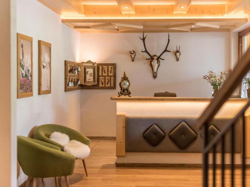 Heller Empfangsbereich mit Holzboden, grünem Sessel, Geweihdeko und warm beleuchtetem Tresen.