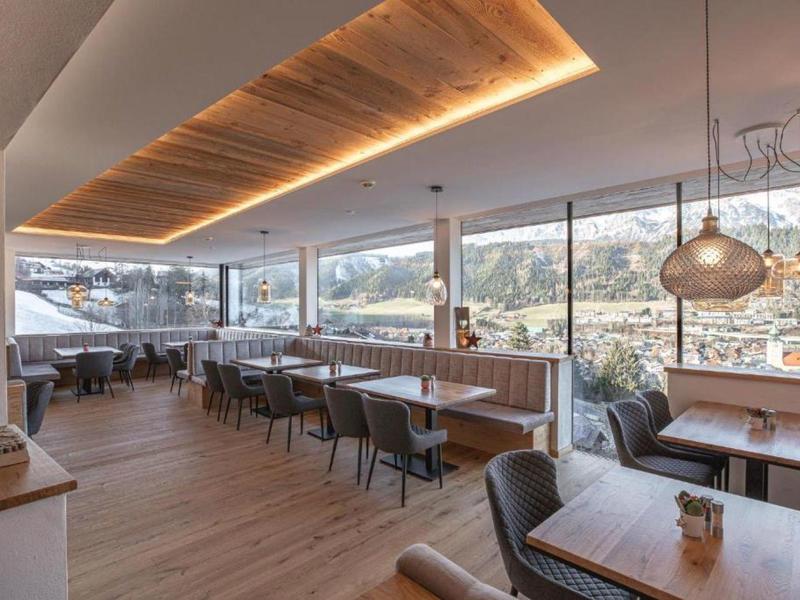 Helles Restaurant mit großen Fenstern, Holzboden, modernen Tischen und Stühlen sowie warmem Deckendetail.