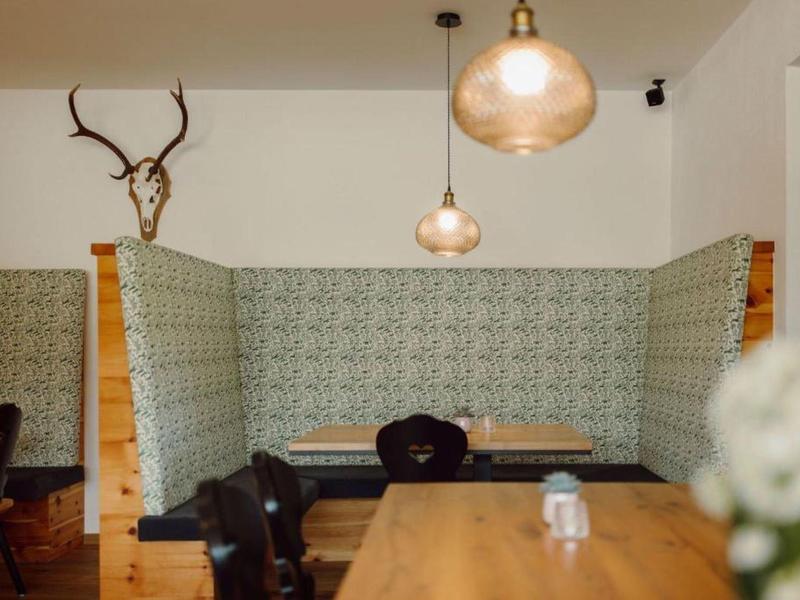 Gemütliche Sitzecke mit gemusterten Wänden, hölzernem Tisch, schwarzen Stühlen und Hirschgeweih-Dekor.