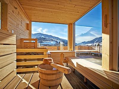 Ein heller Holzsauna mit Panoramafenstern und Blick auf Berge und blauen Himmel.
