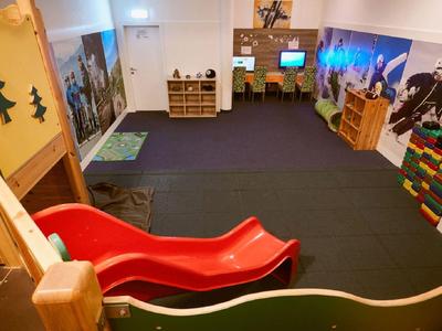 Kinderspielzimmer mit roter Rutsche, buntem Spielzeug und Wandbildern in hellem Raum.
