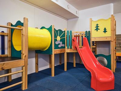 Buntes Indoor-Klettergerüst mit gelbem Tunnel und roter Rutsche auf blauem Boden.