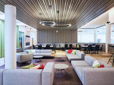 Modernes, helles Büro mit grauen Sofas, bunten Kissen, runden Tischen und Holzdecken mit Lichtringen.