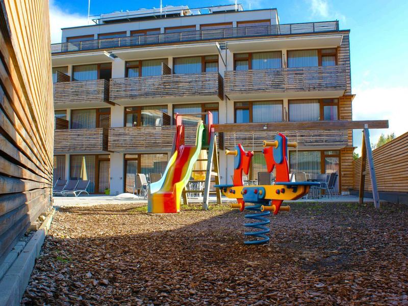 Moderner Kinderspielplatz mit bunten Rutschen vor einem mehrstöckigen Gebäude bei klarem Himmel.