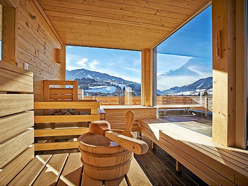 Ein heller Holzsauna mit Panoramafenstern und Blick auf Berge und blauen Himmel.