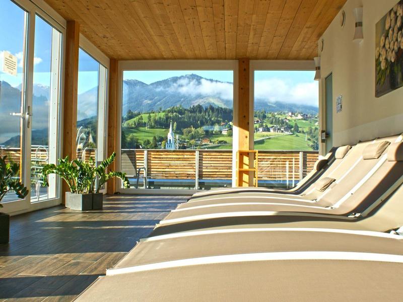 Helle Terrasse mit Holzdecke, Liegestühlen, Pflanzen und Aussicht auf Berge im Sonnenschein.
