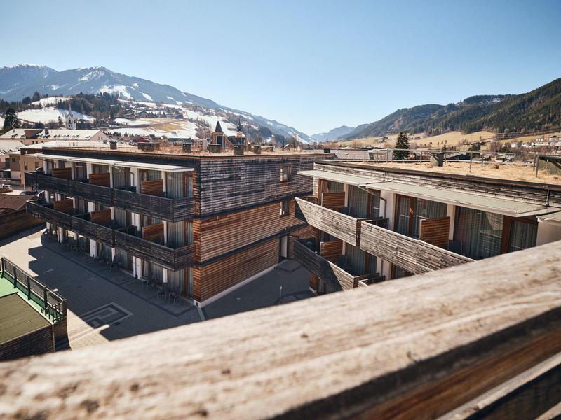 Moderne Holzbauten in Berglandschaft mit klar blauem Himmel und Bergen im Hintergrund.