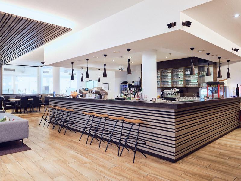 Moderner Cafébereich mit langem Bartresen, vielen Hockern und hellen Holzböden.