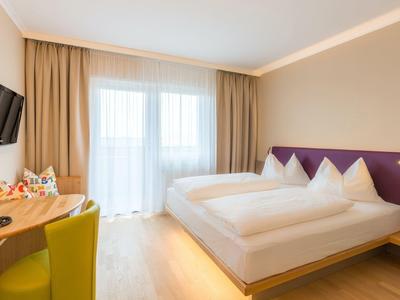 Modernes Hotelzimmer mit Doppelbett, Schreibtisch, Stuhl und großem Fenster mit Vorhängen