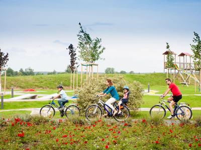 Tři lidé jedou na kole po stezce podél zelené parkové krajiny.