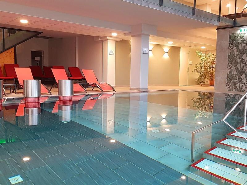 Moderner Innenpool mit blauen Wasserfliesen und roten Liegestühlen.