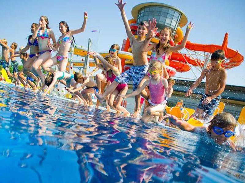 Menschen springen fröhlich in ein Schwimmbecken bei Sonnenschein in einem Wasserpark.