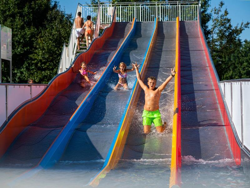 Kinder rutschen auf bunten Wasserrutschen in einem Schwimmbad bei sonnigem Wetter.