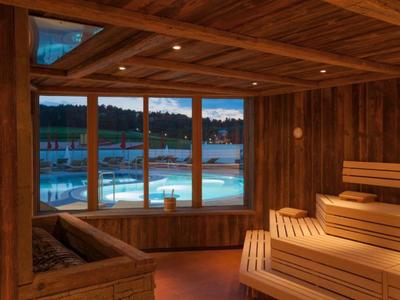 Gemütliche Sauna mit Holzbänken und Blick auf beleuchtetes Schwimmbecken bei Abenddämmerung.