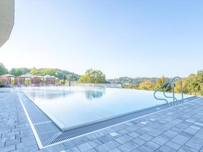 Moderner Außenpool mit klarer Wasserfläche und umliegender Steinfläche, umgeben von grüner Landschaft.