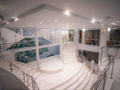 Weißer, moderner Innenraum mit geschwungenen Treppen, Glasgeländern und großen Fenstern.