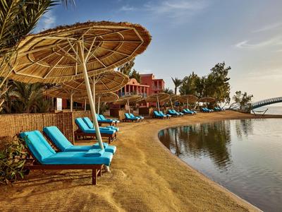 Spiaggia con lettini blu e ombrelloni di paglia vicino a un lago al tramonto
