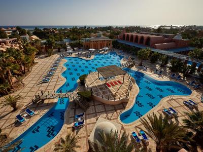 Duży basen hotelowy z parasolami, leżakami i mostkiem nad basenem.