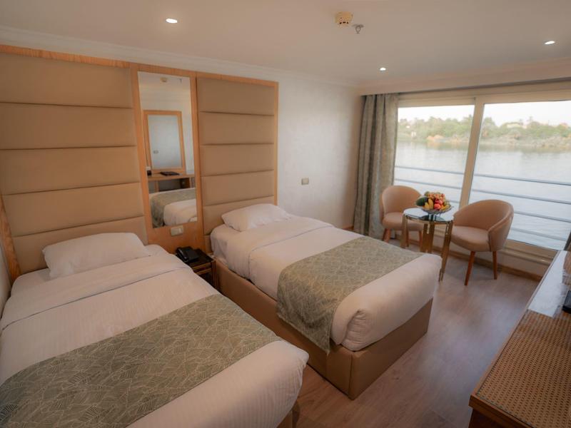 Zweibettzimmer mit Holzdekor, großen Fenstern und Blick auf einen Fluss, zwei Stühle, Nachttisch.