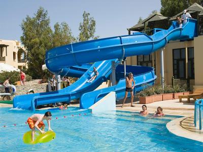 Kinderen spelen in het zwembad met een blauwe glijbaan bij de hotel tuin.