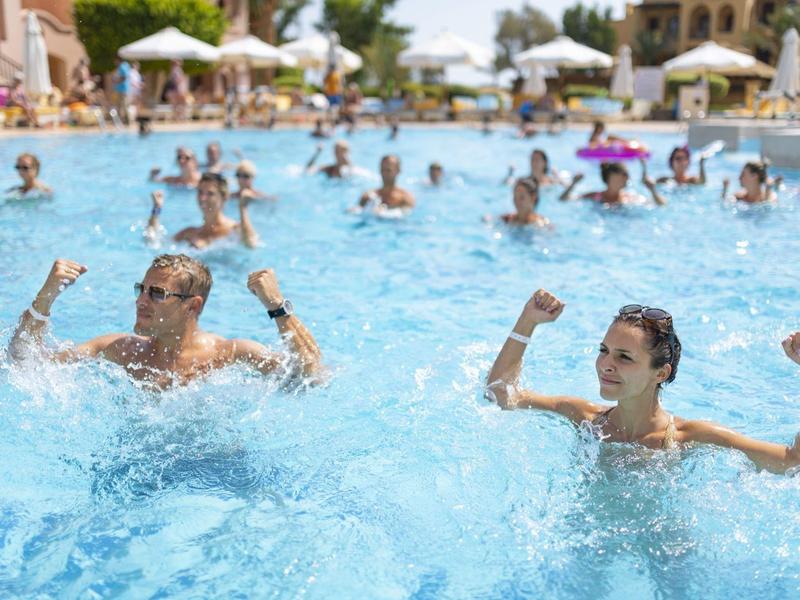 Viele Menschen schwimmen und spielen in einem großen blauen Pool an einem sonnigen Tag.