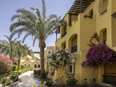 Gelbes Wohnhaus mit Bougainvillea, Palmen und sonnigem Himmel entlang eines gepflasterten Wegs.