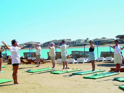 Gruppe von Menschen macht Yoga am Strand mit Handgewichtsgeräten bei sonnigem Wetter.