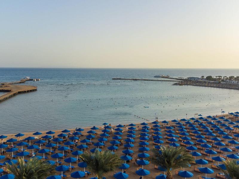 Strand mit vielen blauen Sonnenschirmen und ruhigem Meer im Hintergrund bei Sonnenuntergang.