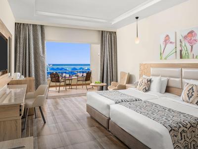 Helles Hotelzimmer mit Doppelbett und Balkon mit Meerblick.