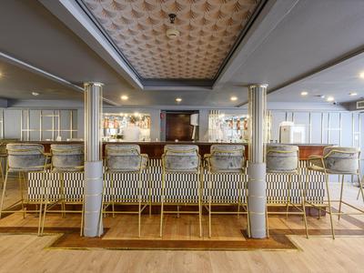 Bar moderne avec des tabourets en métal doré, plafond décoré et éclairage doux.