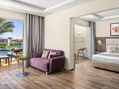 Chambre d'hôtel lumineuse avec lit double, canapé violet et vue sur la piscine.