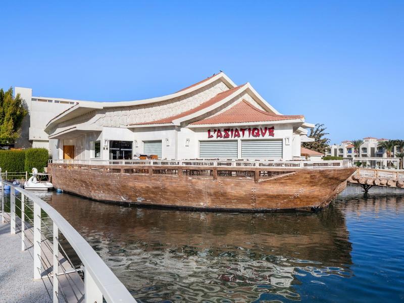 Bâtiment côtier avec un bateau en bois au premier plan sur une eau calme.