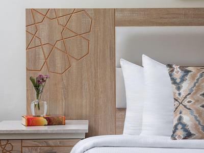 Modern hotel room with wood decor, white pillows, and colorful pillow on the bed.