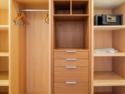 Open beige wooden wardrobe with drawers, shelves, hangers, microwave, and safe.